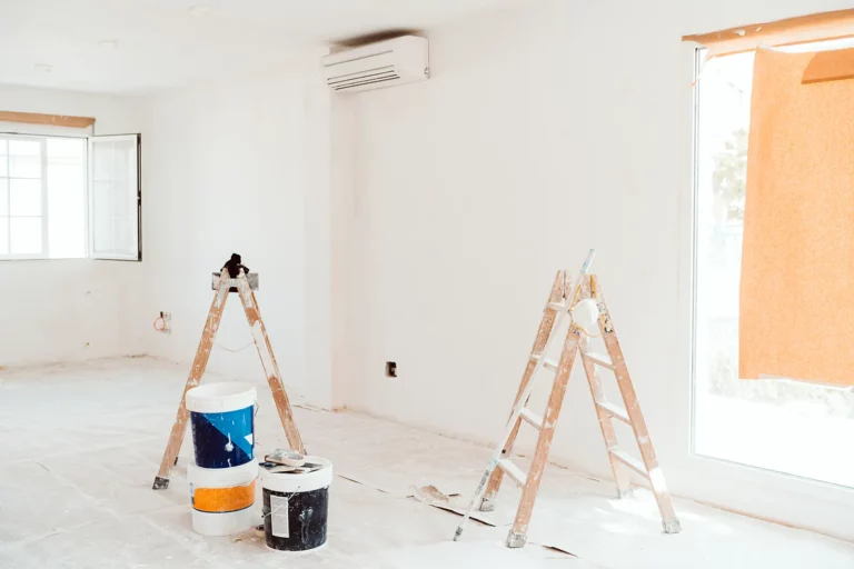 two stepladders and buckets of paint on the floor in the room where the walls are being painted